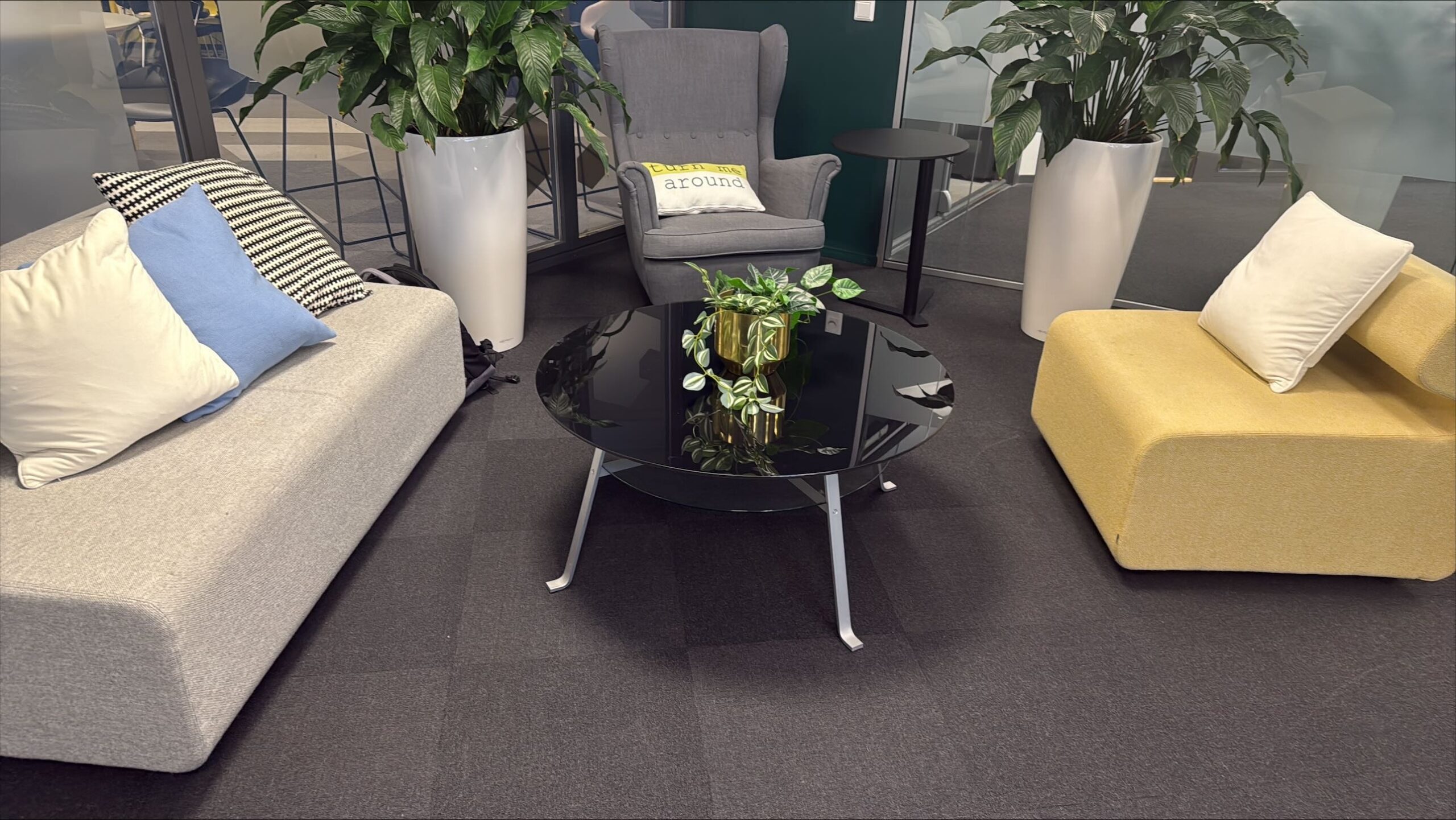 Office lounge with grey sofa groups, yellow cushions and plants