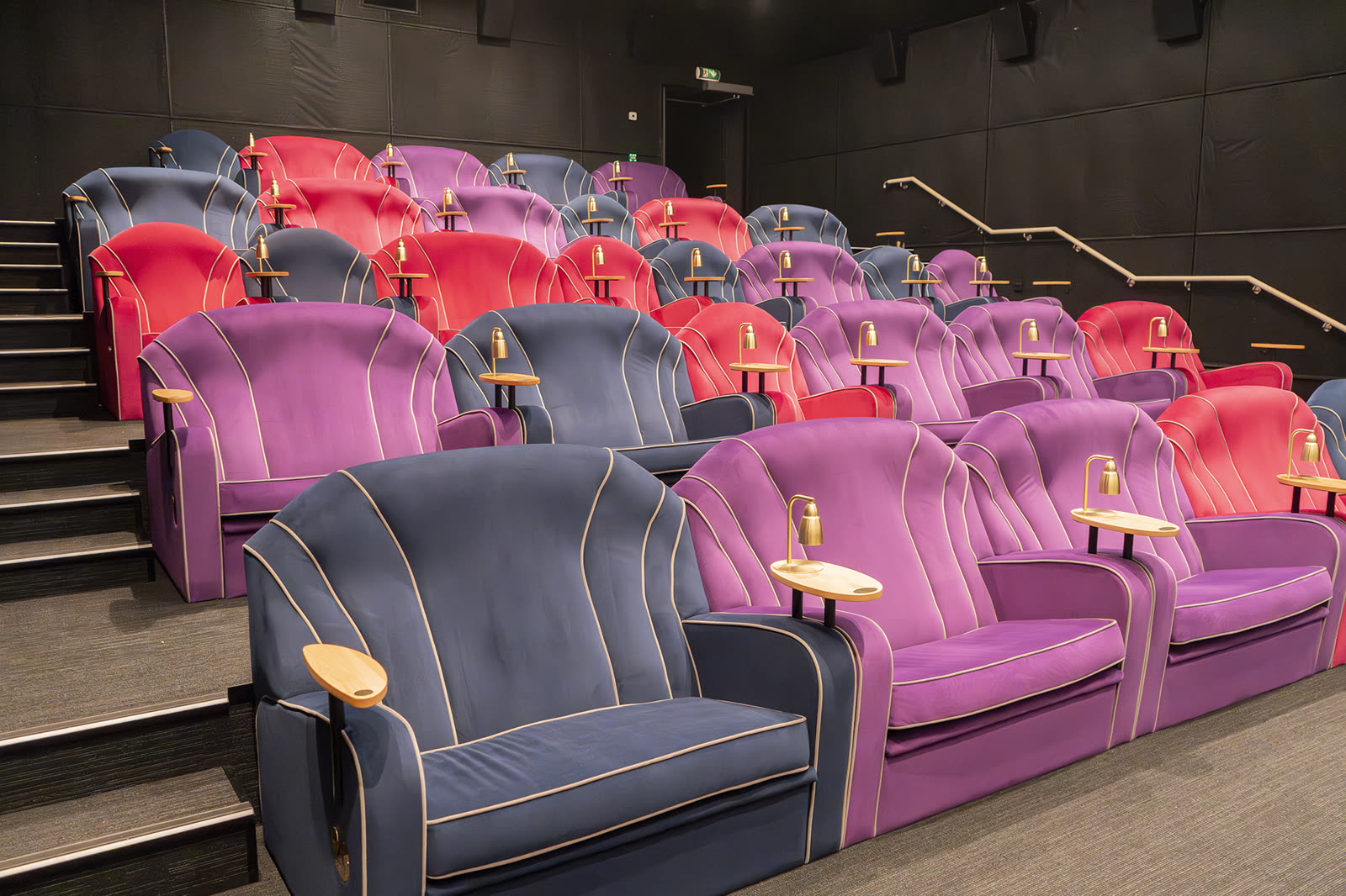 Premium recliner auditoriums with red, purple and blue velour seats